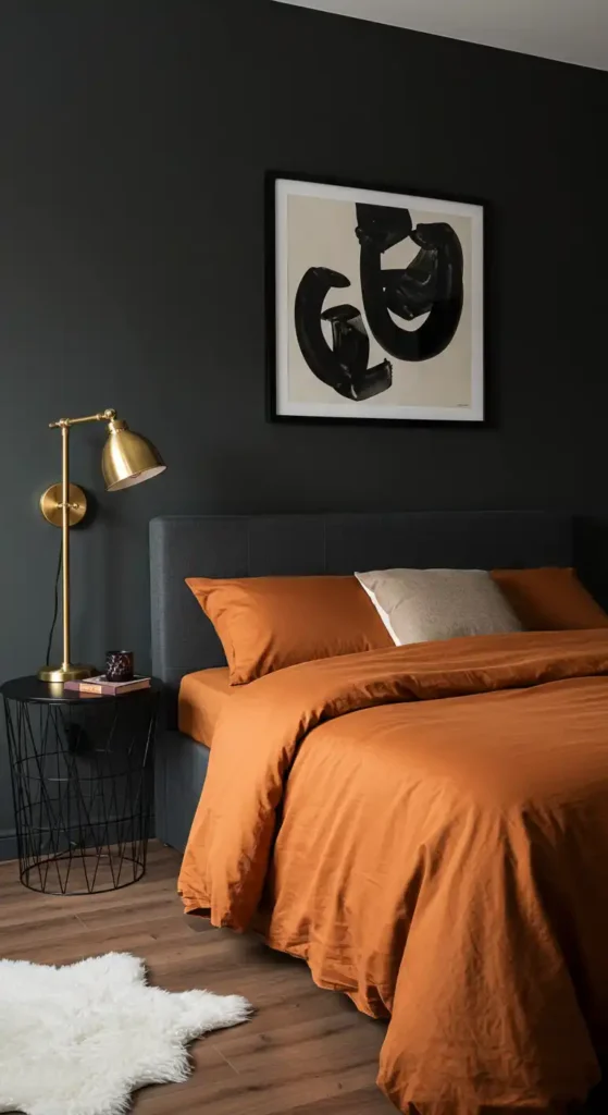 Modern bedroom with charcoal walls, burnt orange bedding, brass lamps, black-framed art, and white rug.